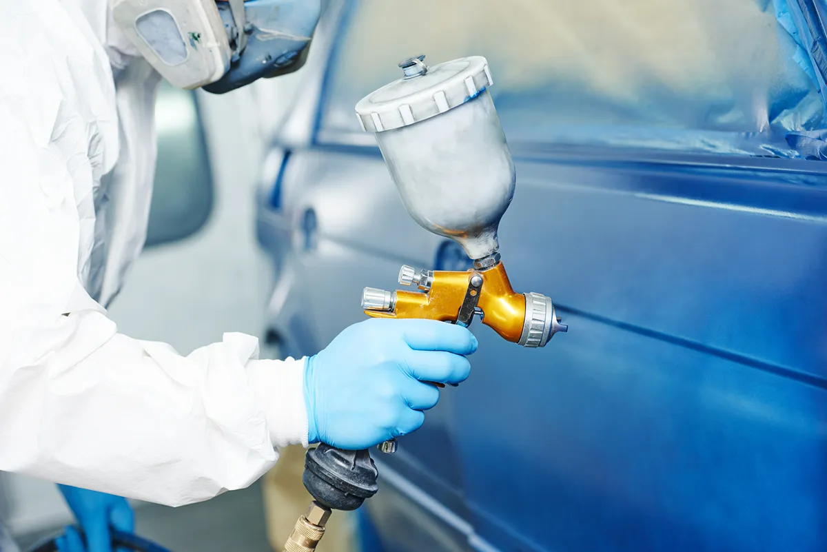 Auto body technician painting a blue car