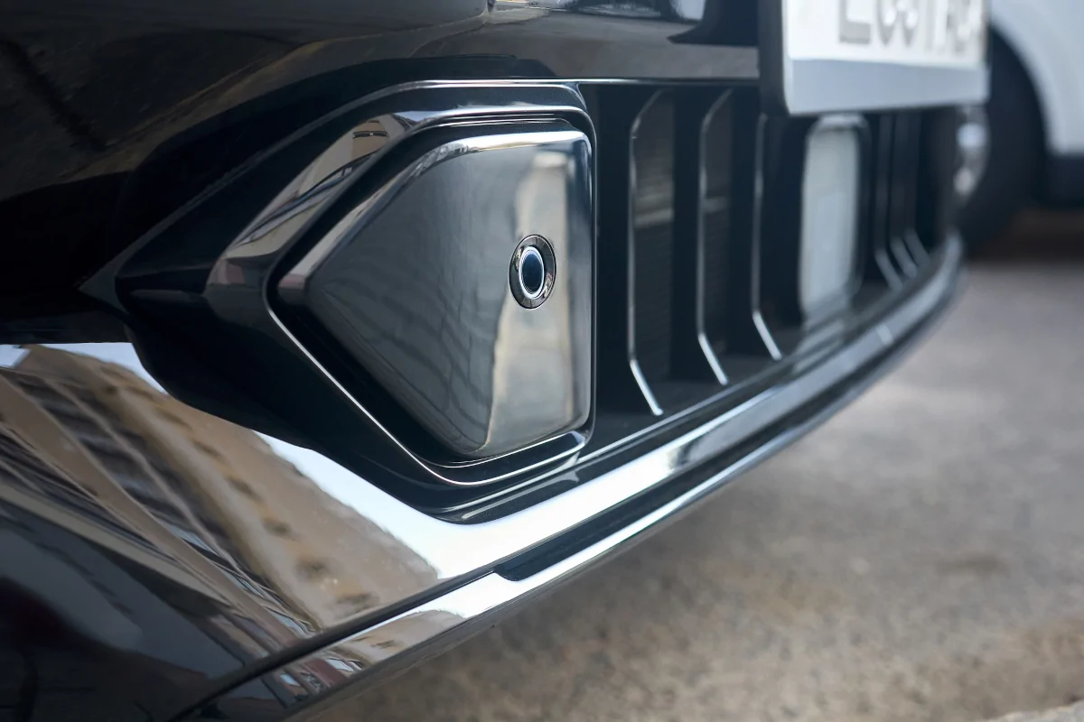 Close-up of a vehicle bumper with a parking sensor built into the painted bumper cover.