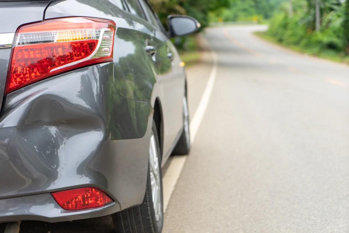 Rear bumper damage on a gray vehicle parked along the side of a road.